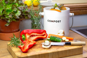 Food waste recycling in kitchen, food waste from food preparation collected for recycling in kitchen compost collecting pot container with chopped vegetables with knife on chopping board