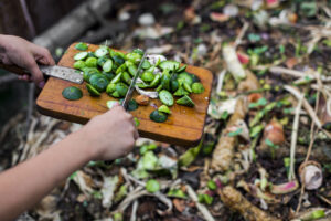 child's hands throwing out kitchen waste from the vintage cutting board to the garden compost heap for recycling and fertilizer