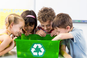 Cute children looking at plastic bottles in recycling box in classroom