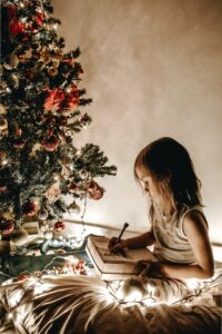 Little girl writing, next to a Christmas tree